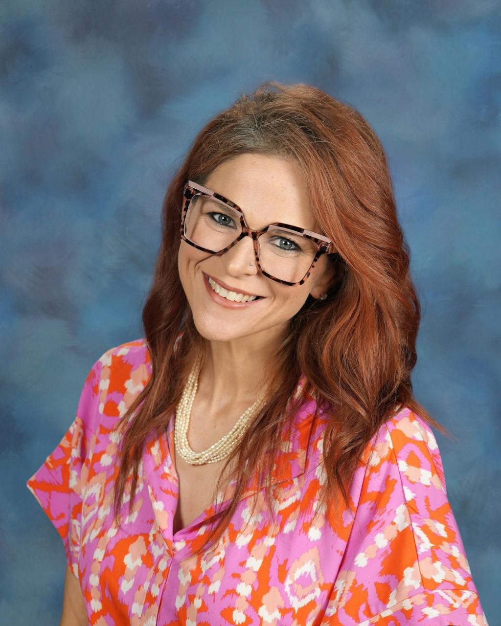 Lady wearing glasses with a colorful pink top, and a necklace